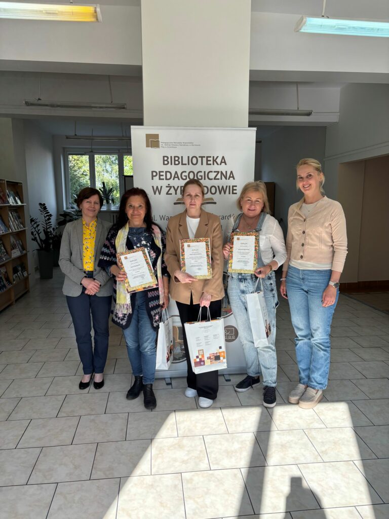 Zdjęcie przedstawia pięć kobiet z dyplomami i nagrodami za udział w konkursie w pomieszczeniu biblioteki.